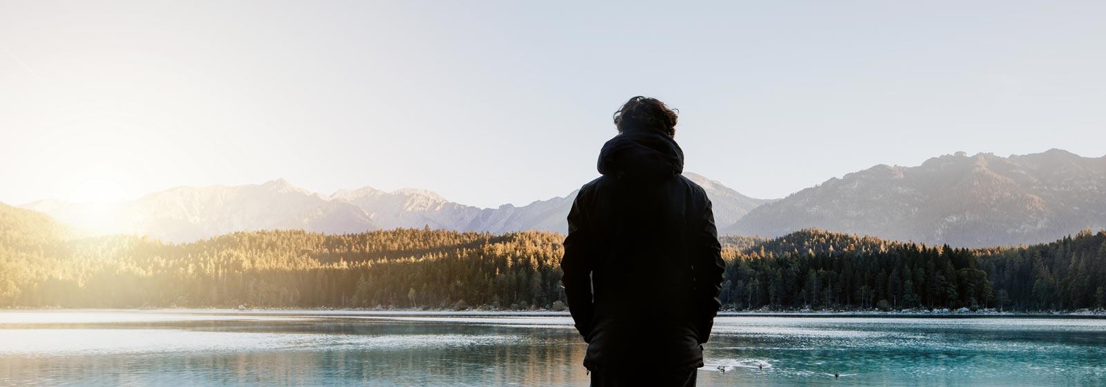 Ein Mann steht am Ufer des Sees und schaut nackdenklich in die Ferne.